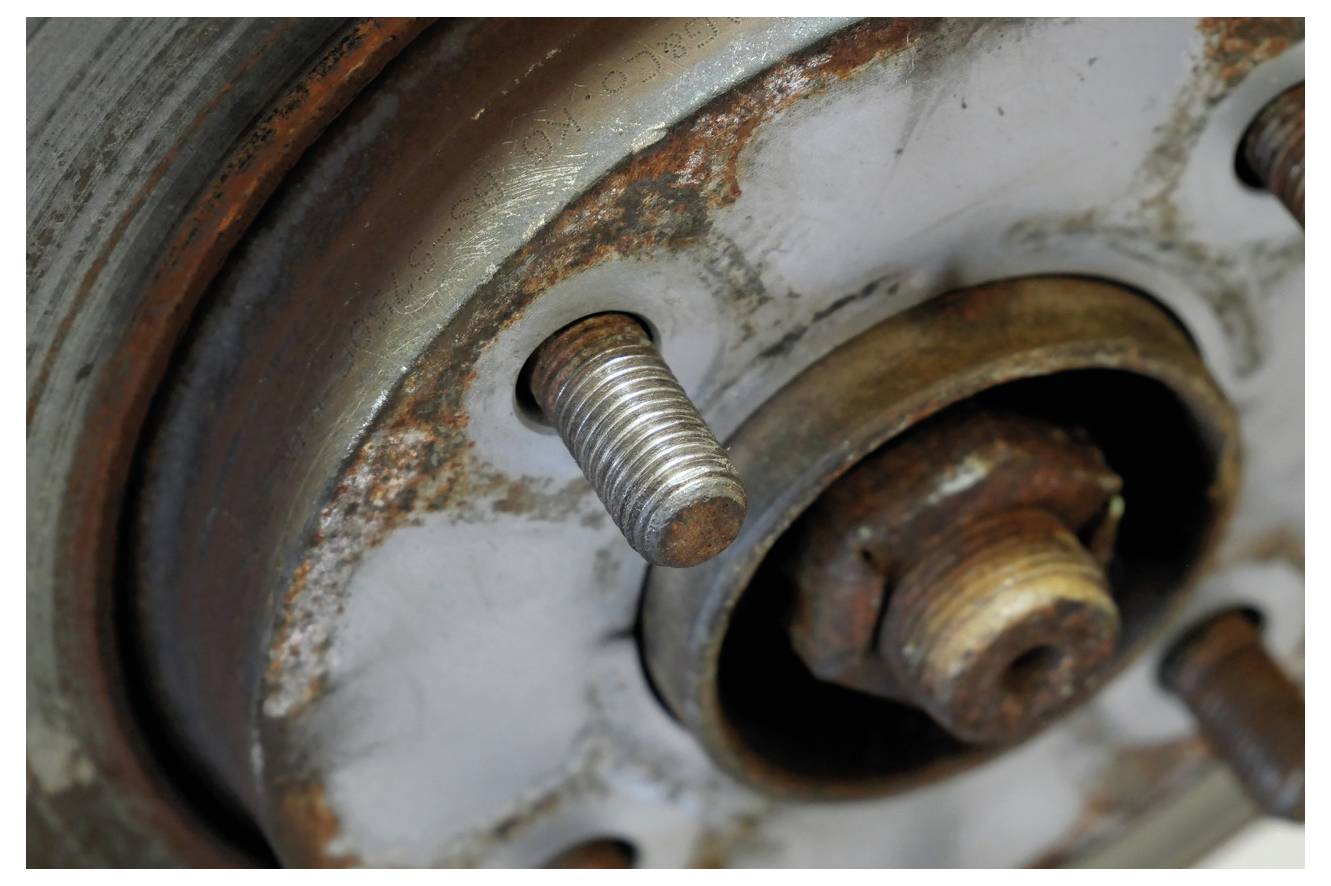 Bolzen und verrosteter Bereich auf einer Metalloberfläche, möglicherweise Teil einer Fahrzeugrad-Baugruppe. Zeigt Verschleiß und Korrosion.