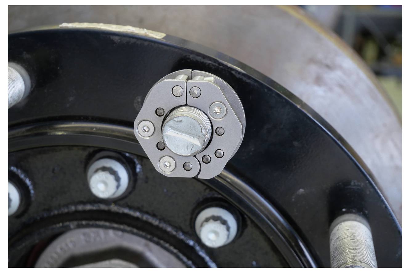 Eine Nahaufnahme eines mechanischen Bauteils mit einem kreisförmigen schwarzen Teil mit silbernen Bolzen und einem zentralen silbernen sechskantigen Stück, möglicherweise ein Industriemaschinenteil.