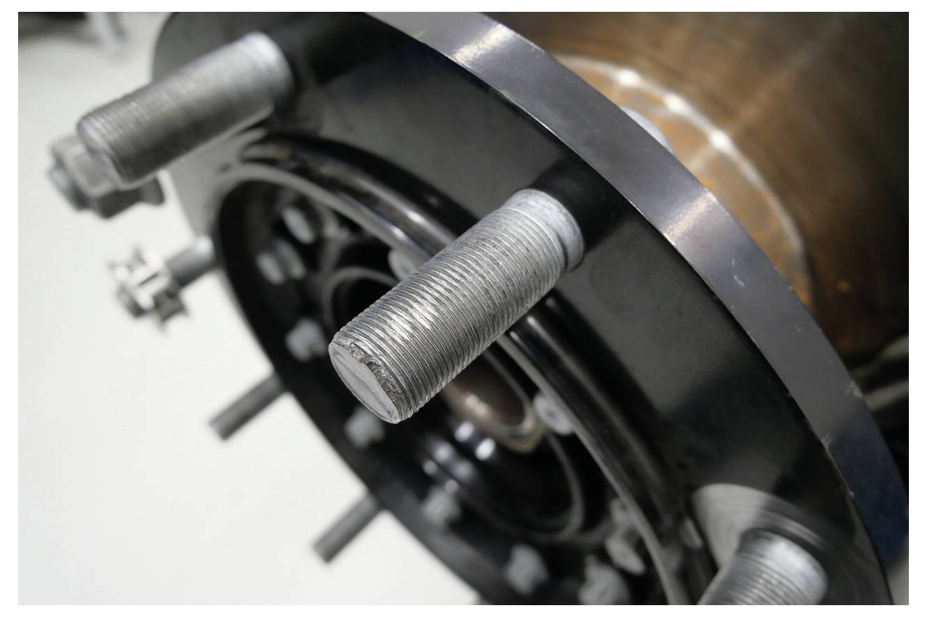 Nahaufnahme einer Metallradnabe mit sichtbaren Gewindelbolzen und glänzenden schwarzen und braunen Komponenten, die auf einen Maschinen- oder Ingenieurkontext hindeuten.