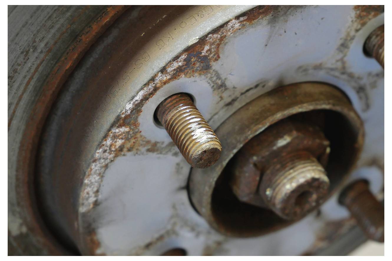 Eine Nahaufnahme einer verrosteten Autobremsflansche und Radnabe mit freiliegenden Radbolzen. Die Metalloberfläche zeigt Anzeichen von Korrosion und Verschleiß.