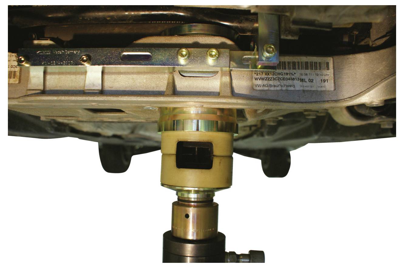 Nahaufnahme des Unterbodens eines Fahrzeugs mit Fokus auf eine zu reparier- oder inspizier- ende Komponente, die mechanische Teile und ein eingesetztes Werkzeug zeigt.