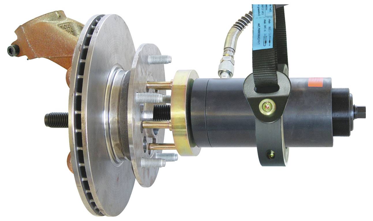 Ein Werkzeug, das mit einem Riemen und Bolzen an einem Bremsrotor eines Autos befestigt ist. Die Anordnung scheint für Test- oder Wartungszwecke konzipiert zu sein.