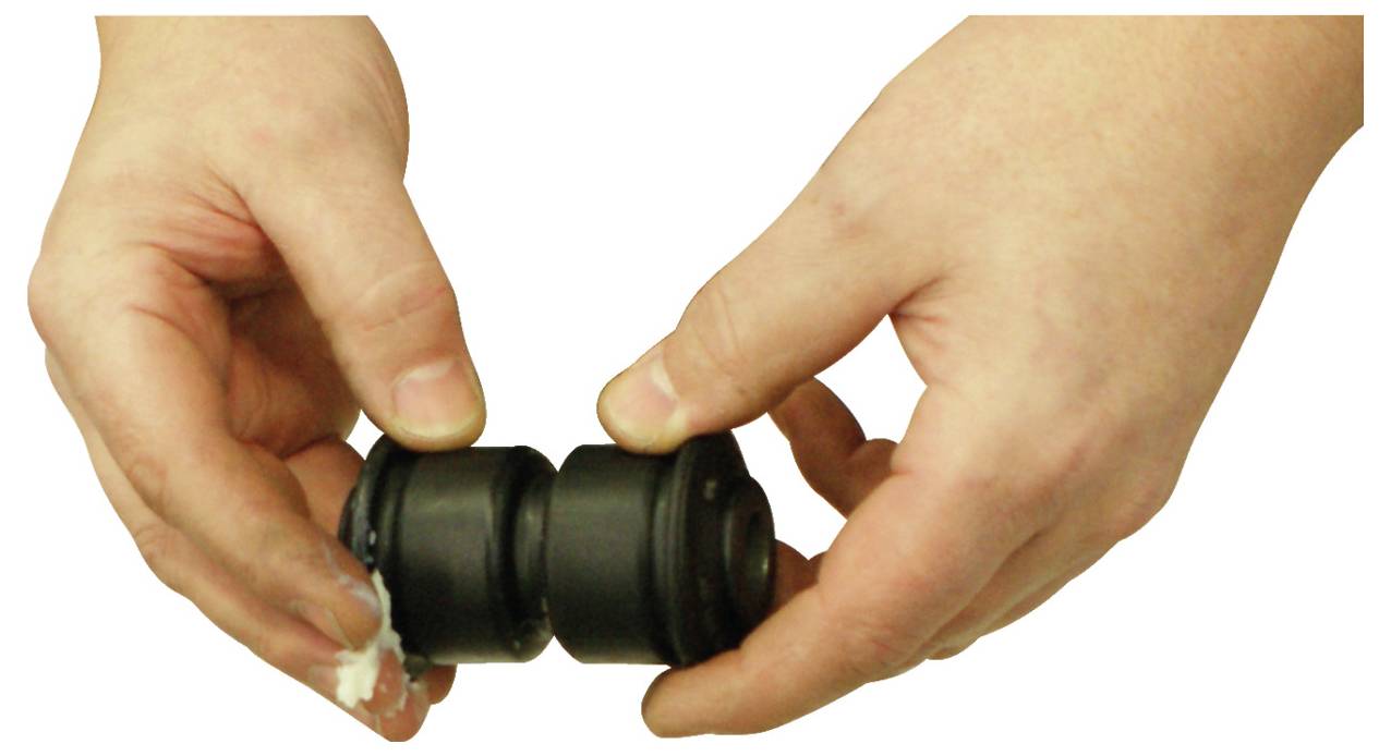 Zwei Hände halten ein kleines schwarzes zylindrisches Objekt mit Rillen, das einem Automobil- oder Maschinenteil ähnelt.