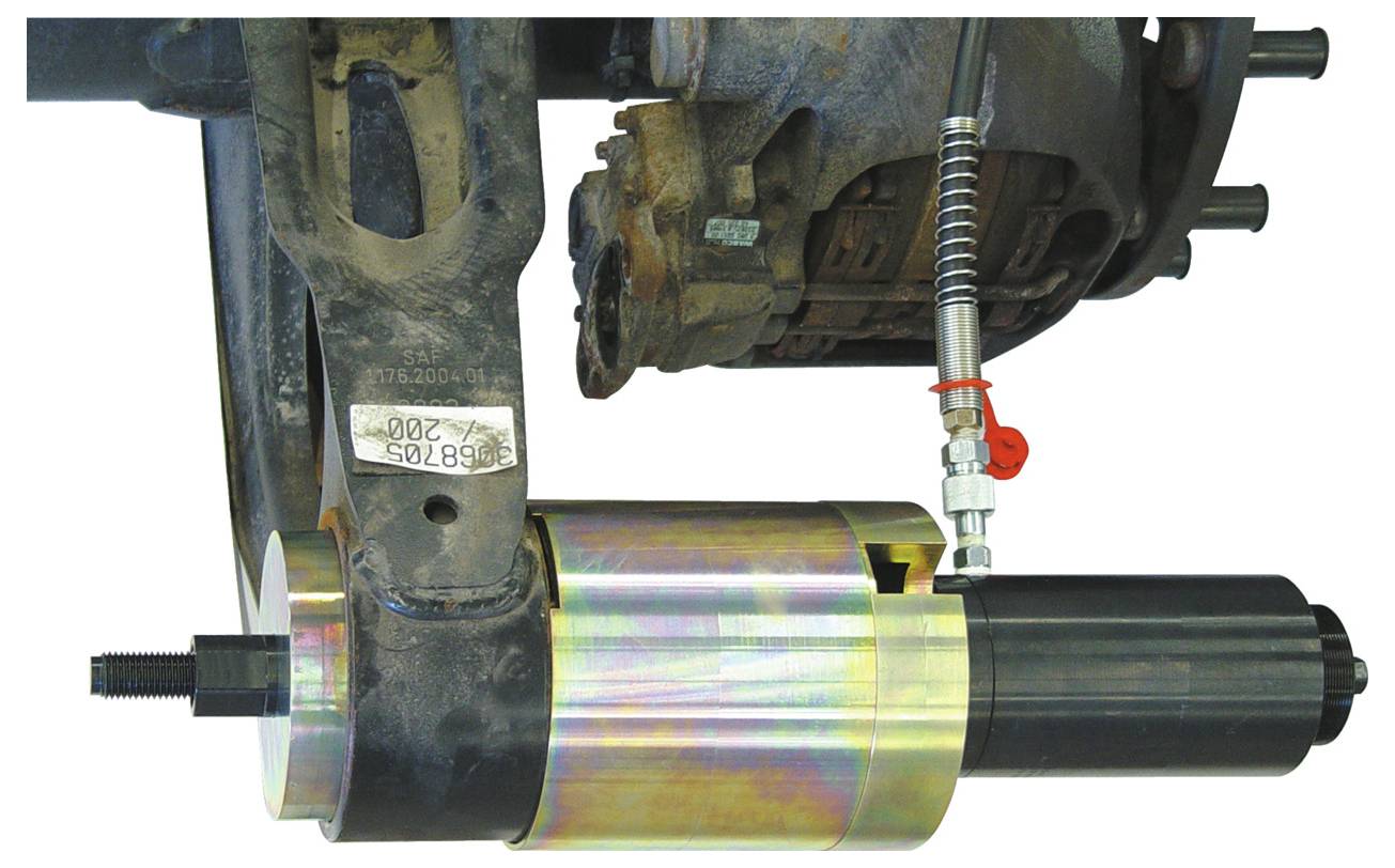 Ein mechanisches Werkzeug, das an einem Aufhängungsarm eines Fahrzeugs befestigt ist, das einen Prozess oder Mechanismus veranschaulicht, der möglicherweise mit der Fahzeugreparatur oder Wartung verbunden ist.