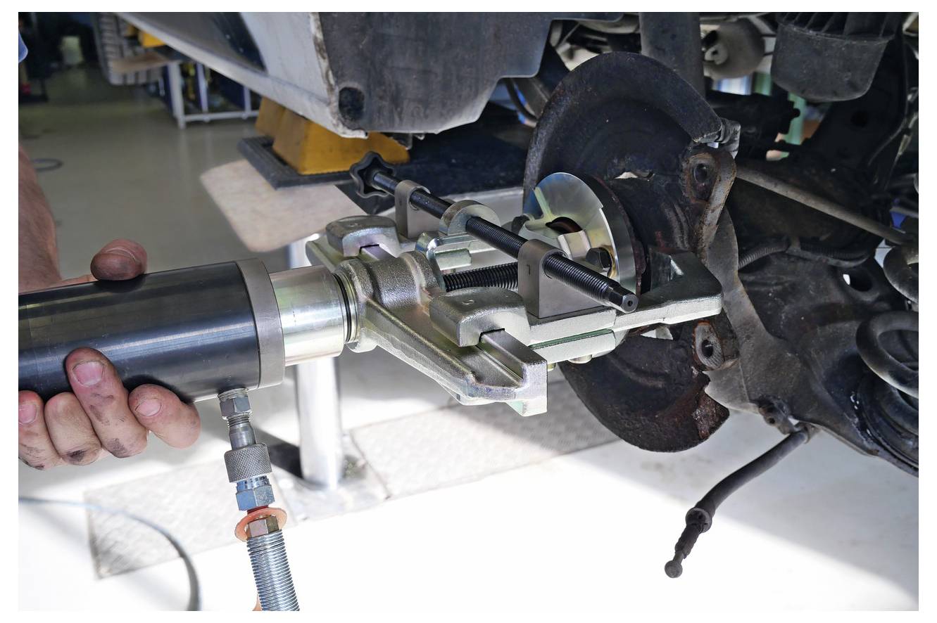 Ein Mechaniker benutzt ein hydraulisches Werkzeug, um eine Radnabe von einem Fahrzeug zu entfernen, wobei der Prozess der Autowartung oder Reparatur veranschaulicht wird.
