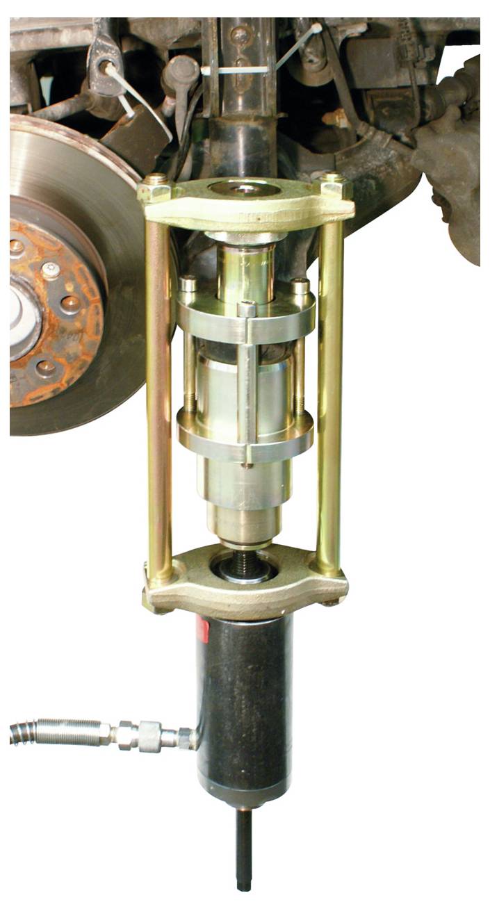 Ein hydraulischer Spulenfedern-Kompressor an einem Aufhängungsstrebe eines Autos angebracht, mit einer sichtbaren Bremsscheibe im Hintergrund.