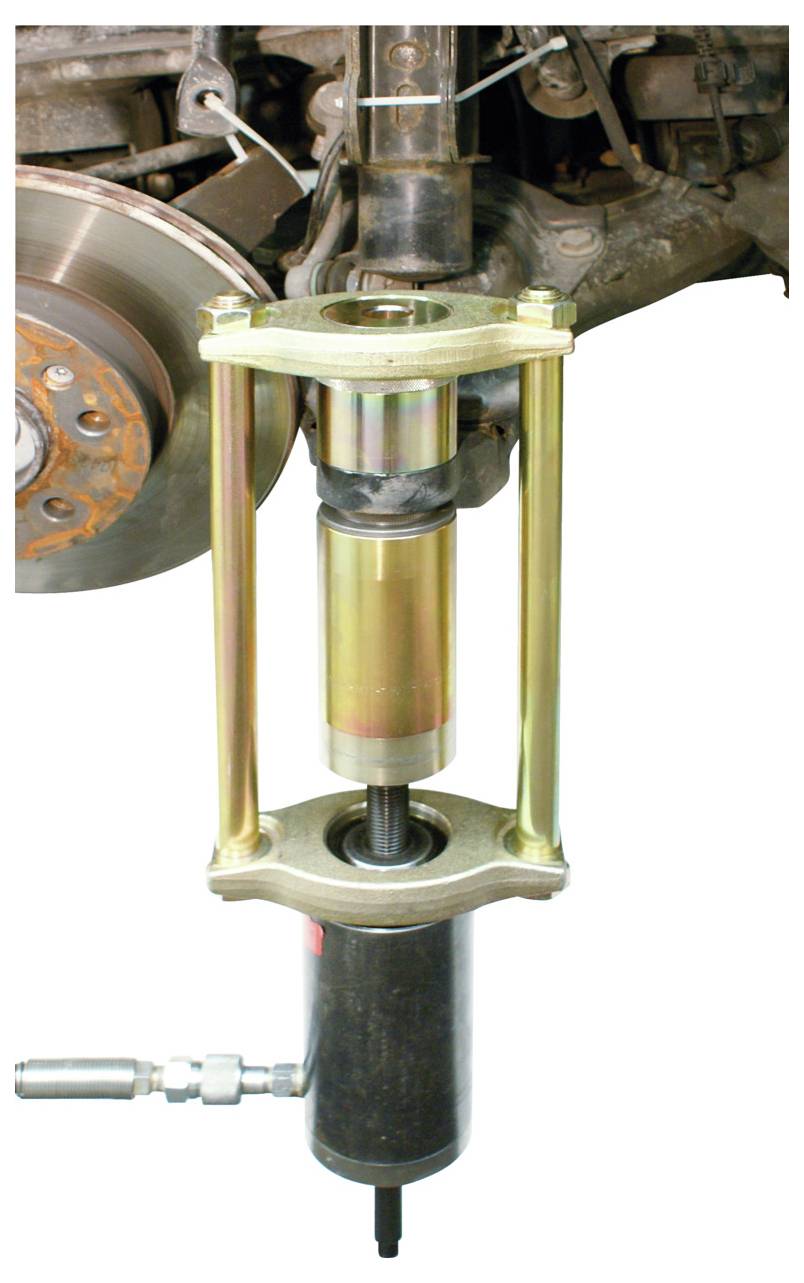 Ein Hydraulikpressen-Werkzeug wird verwendet, um eine Federung in einem Fahrzeug zu komprimieren. In der Nähe ist eine Bremsscheibe teilweise sichtbar.