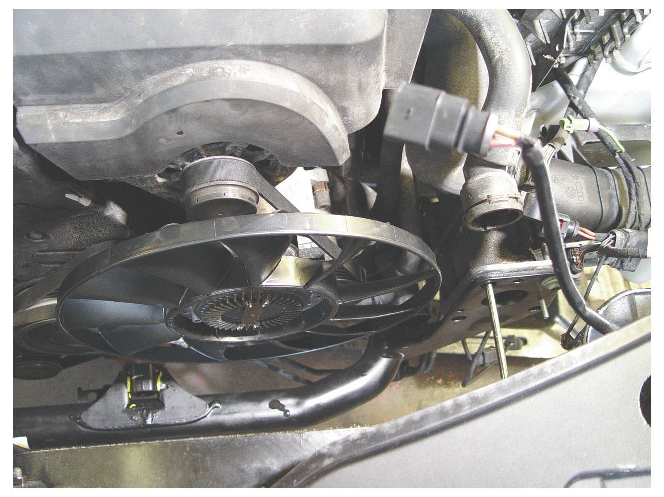 Nahaufnahme eines Automotors mit sichtbarem Kühlventilator und elektrischen Leitungen. Der schwarze Ventilator hat mehrere Blätter und ist zentral angeordnet.