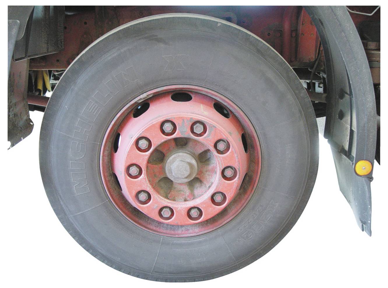 Ein großer schwarzer Reifen, auf einer roten Metallfelge montiert, die an der Unterseite eines Fahrzeugs befestigt ist.