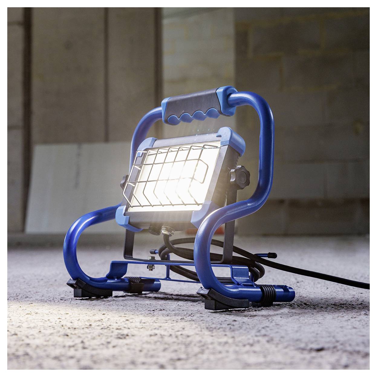 Ein tragbares blaues LED-Arbeitleuchte auf einem Stativ strahlt hell auf einem Betonboden.