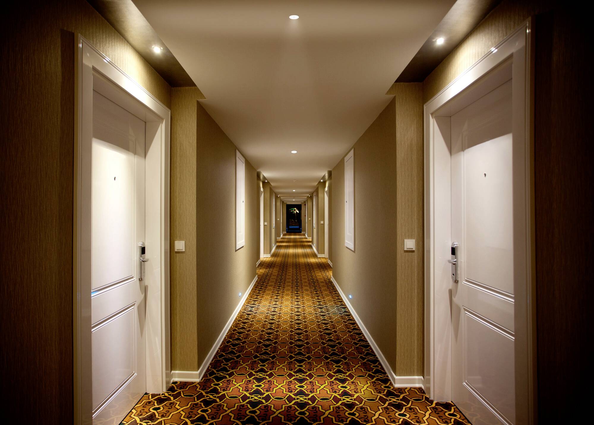 Ein langer Hotelflur mit gemustertem Teppich, weißen Türen auf jeder Seite und warmer Beleuchtung, die eine einladende Atmosphäre schafft.