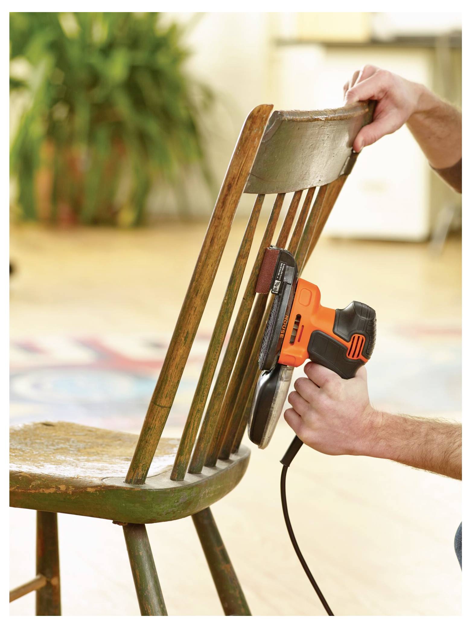 Eine Person verwendet einen elektrischen Schleiffer auf einem Holzstuhl und glättet die Oberfläche. Die Szene deutet auf Heimwerkerarbeiten oder Möbelrestaurierung hin.