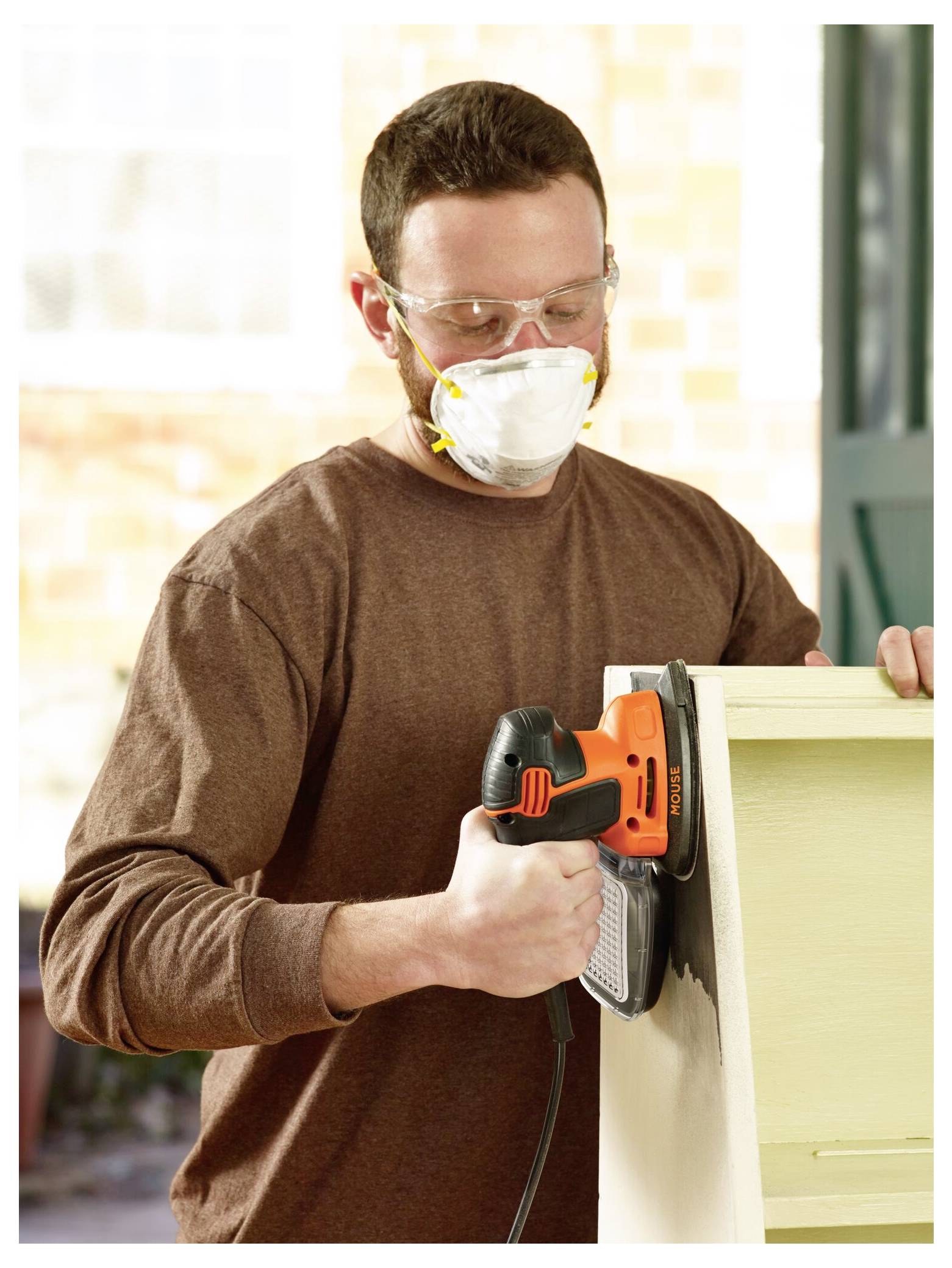 Eine Person, die eine Schutzbrille und eine Maske trägt, verwendet einen elektrischen Schleiffer auf einer Holzoberfläche und hebt eine Heimwerkeraktivität hervor.