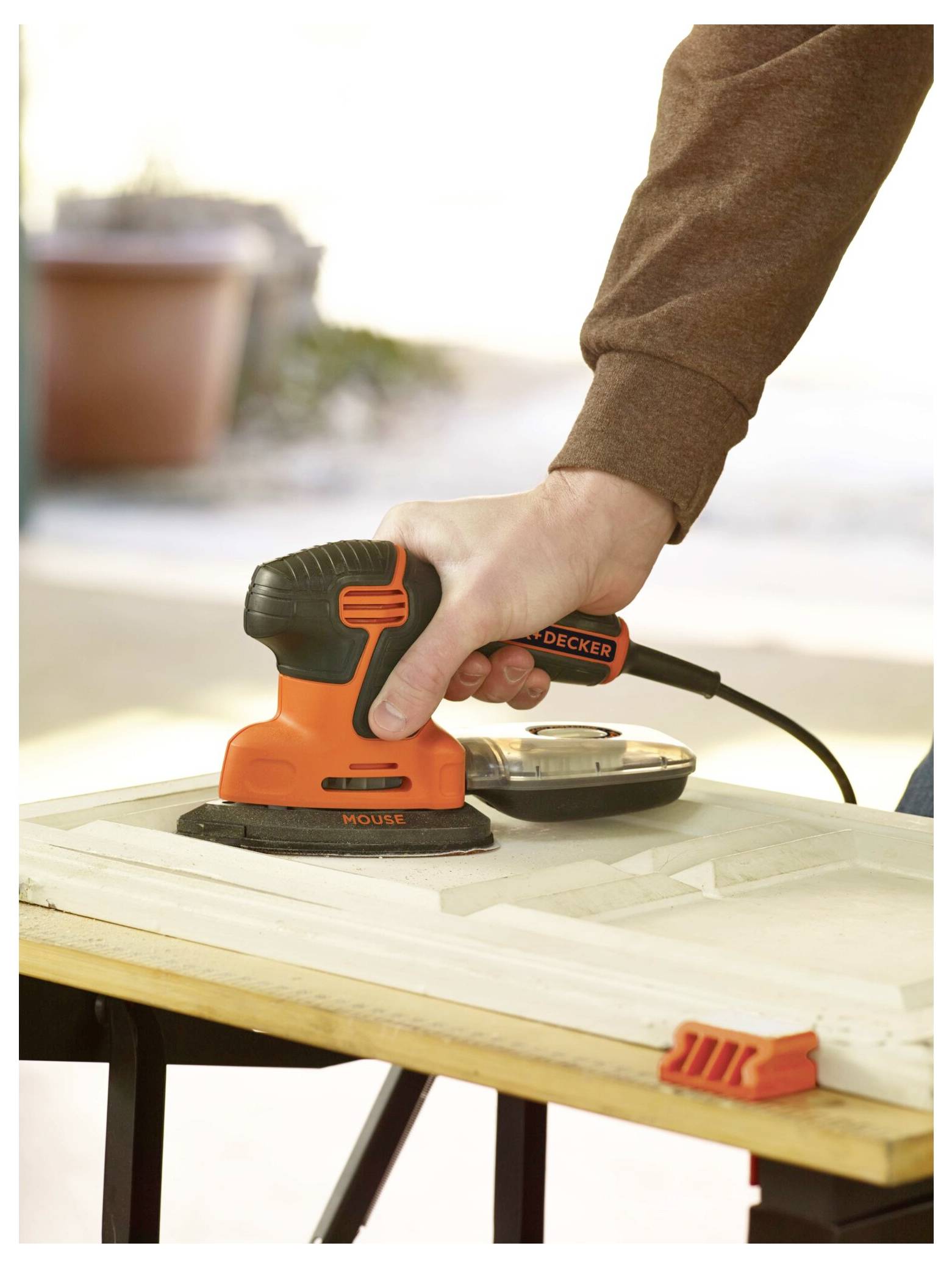 Eine Person, die einen orange-schwarzen tragbaren Elektroschleifers auf einer Holzoberfläche verwendet, demonstriert eine Heimwerker- oder DIY-Aktivität.