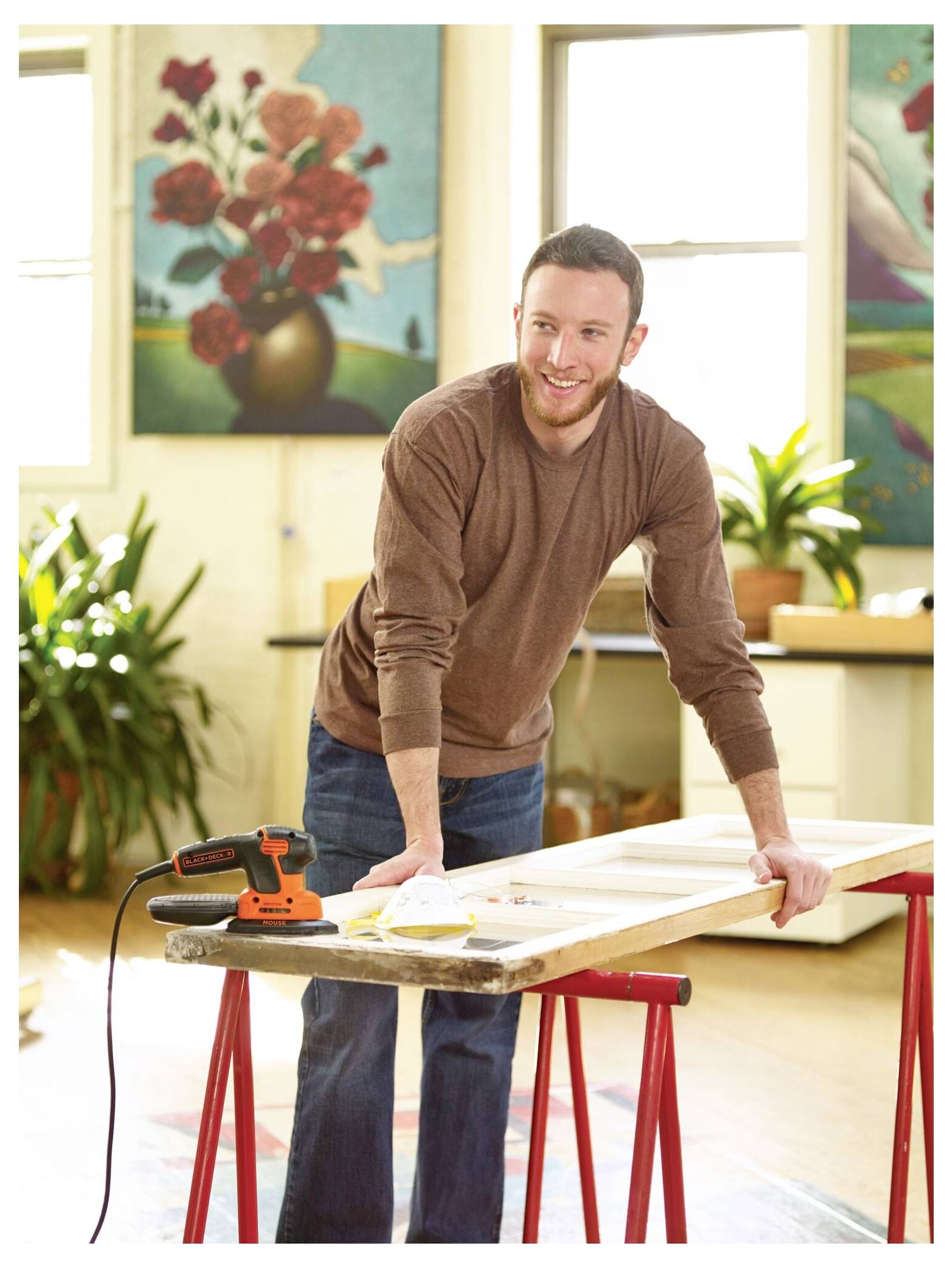 Eine Person, die eine orange-schwarze Kettensäge benutzt, um einen großen Baumstamm auf einem metallischen Sägebock in einem grasbewachsenen Garten durchzutrennen.