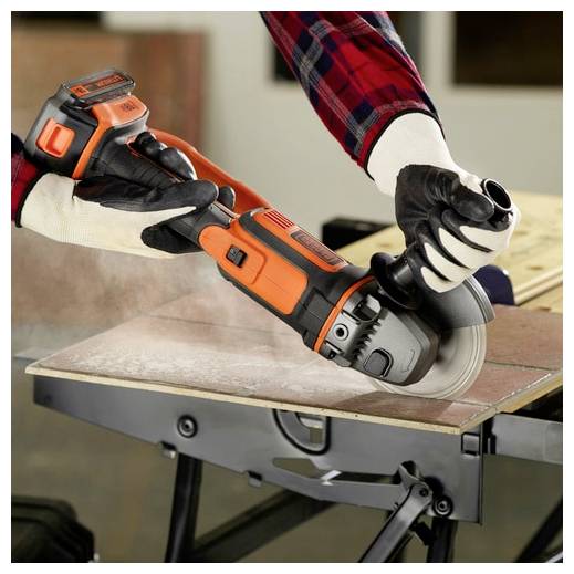 Eine Person mit Handschuhen benutzt einen orange-schwarzen kabellosen Winkelschleifers um ein Stück Holz auf einer Werkbank zu schneiden und demonstriert damit Zimmermannsfertigkeiten.