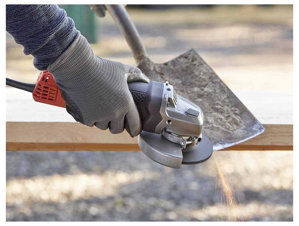 Eine Person trägt Handschuhe und benutzt einen Winkelschleifer, um die Kante einer Schaufel draußen zu schärfen.