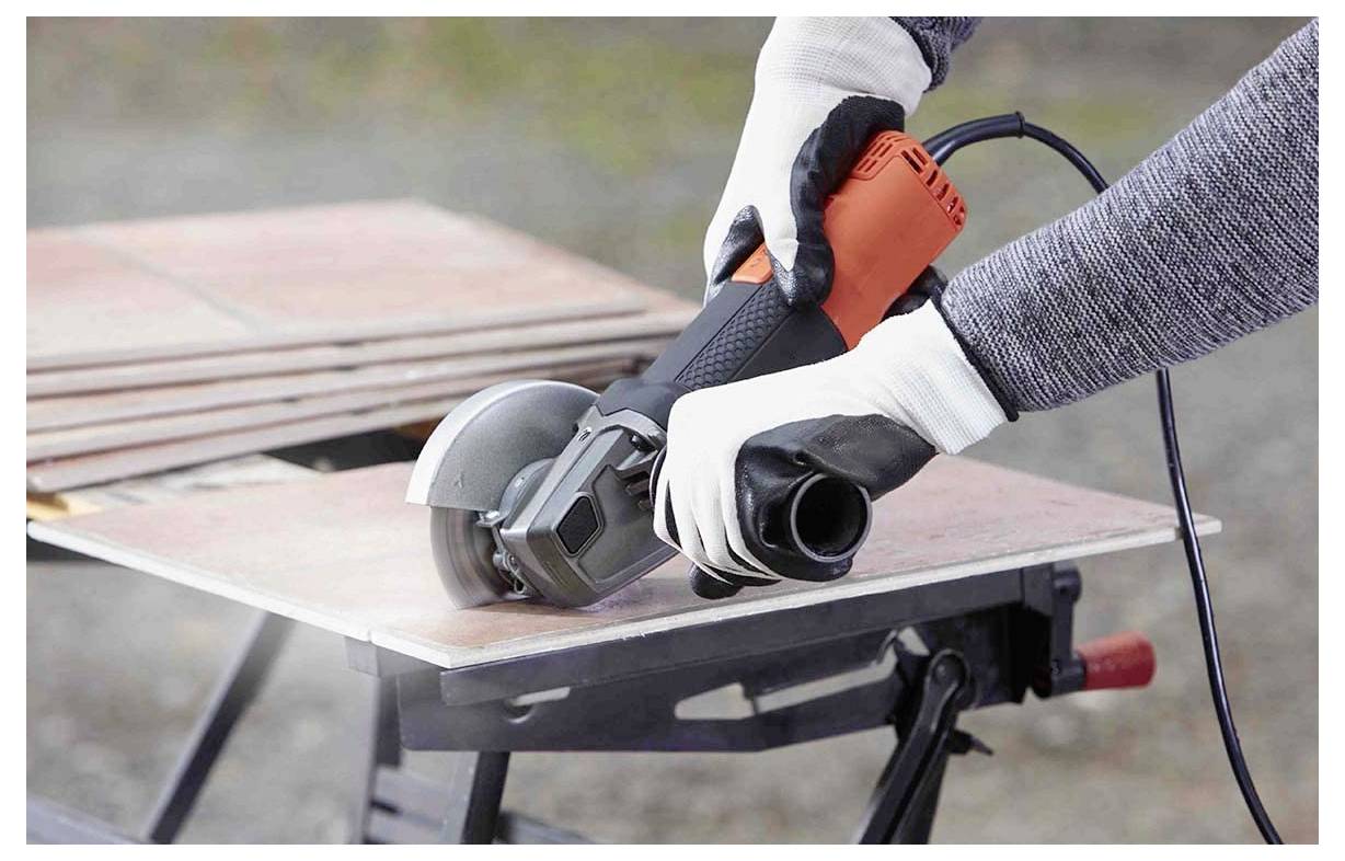 Ein Mann benutzt einen Laubblaspfahl auf einem grasbewachsenen Hof, umgeben von hohen Bäumen und einem kleinen Holzschuppen, unter einem teilweise bewölkten Himmel.