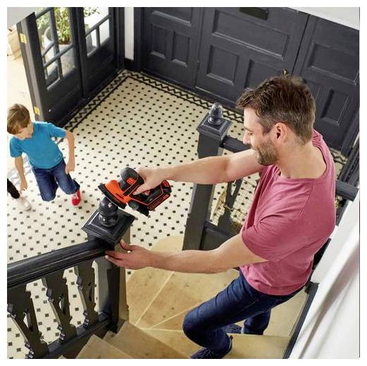 Ein Mann schleimt eine Treppenschranke mit einem elektrischen Schleifergerät, während ein Kind mit roten Schuhen und einem blauen Hemd die Treppe hinaufgeht.