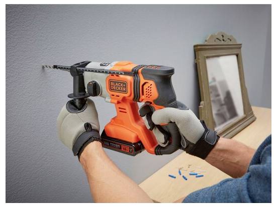 Eine Nahaufnahme eines schwarzen und orangefarbenen Rasentrimmers, der dickichte grüne Unkräuter in einem Garten durchschneidet und zeigt die Schnittbewegung.