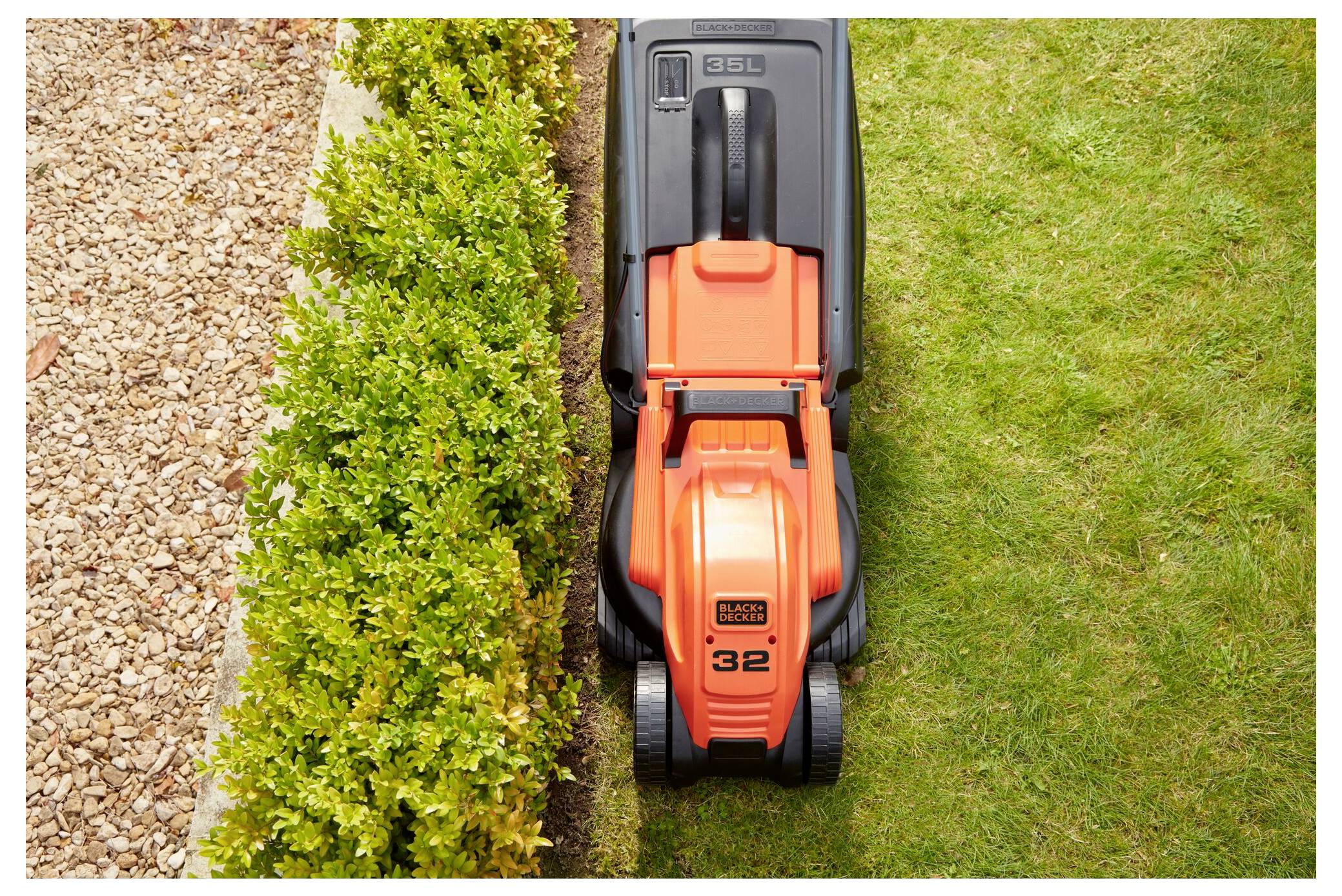 Rasenmäher, der Gras entlang der Kante einer ordentlich geschnittenen Hecke mäht, mit Kies auf der linken Seite und einer deutlich sichtbaren Linie von geschnittenem Gras.