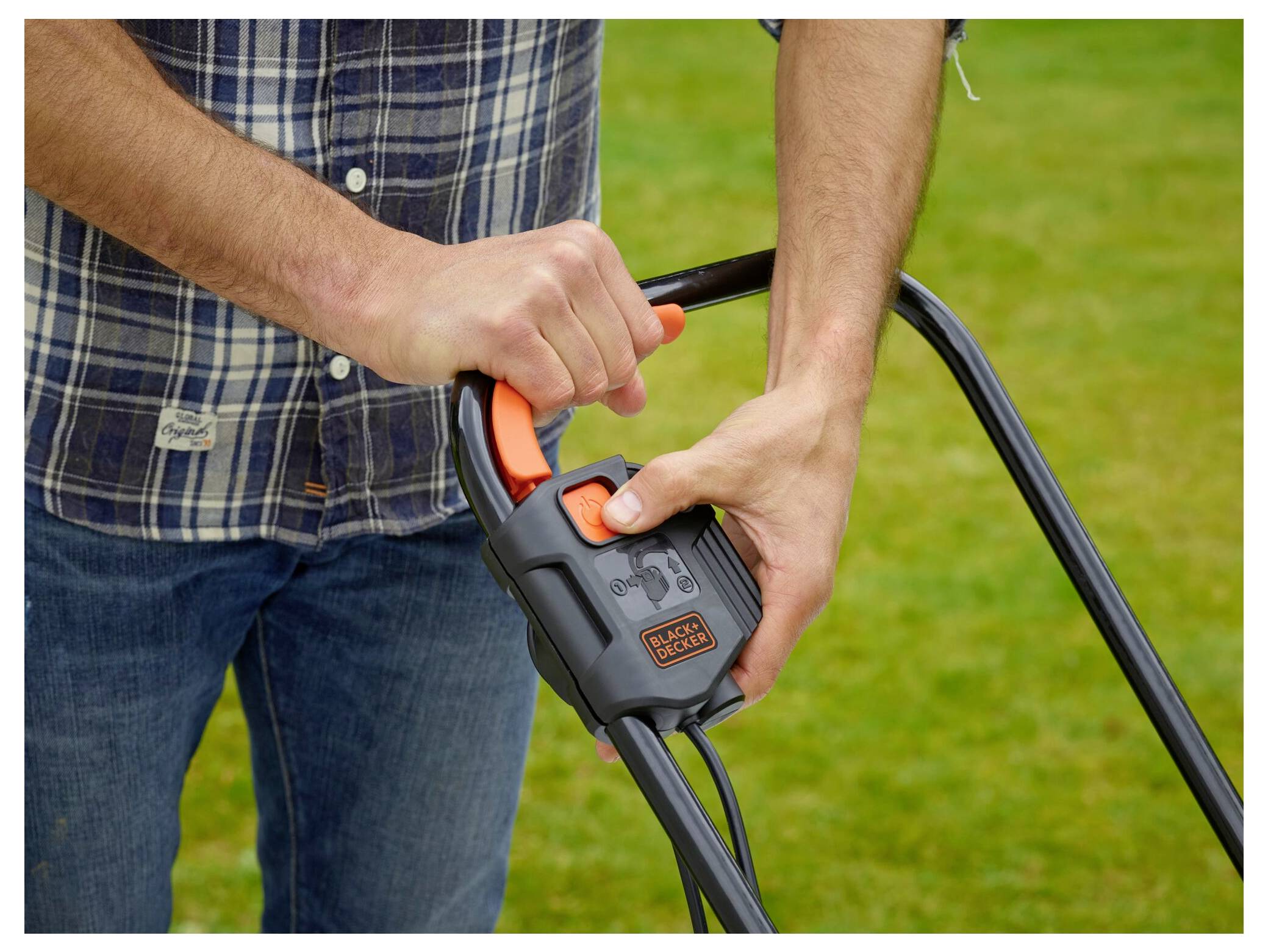 Eine Person hält den Griff eines Rasenmähers und drückt einen orangefarbenen Knopf, um ihn zu starten. Der Hintergrund zeigt grünes Gras.