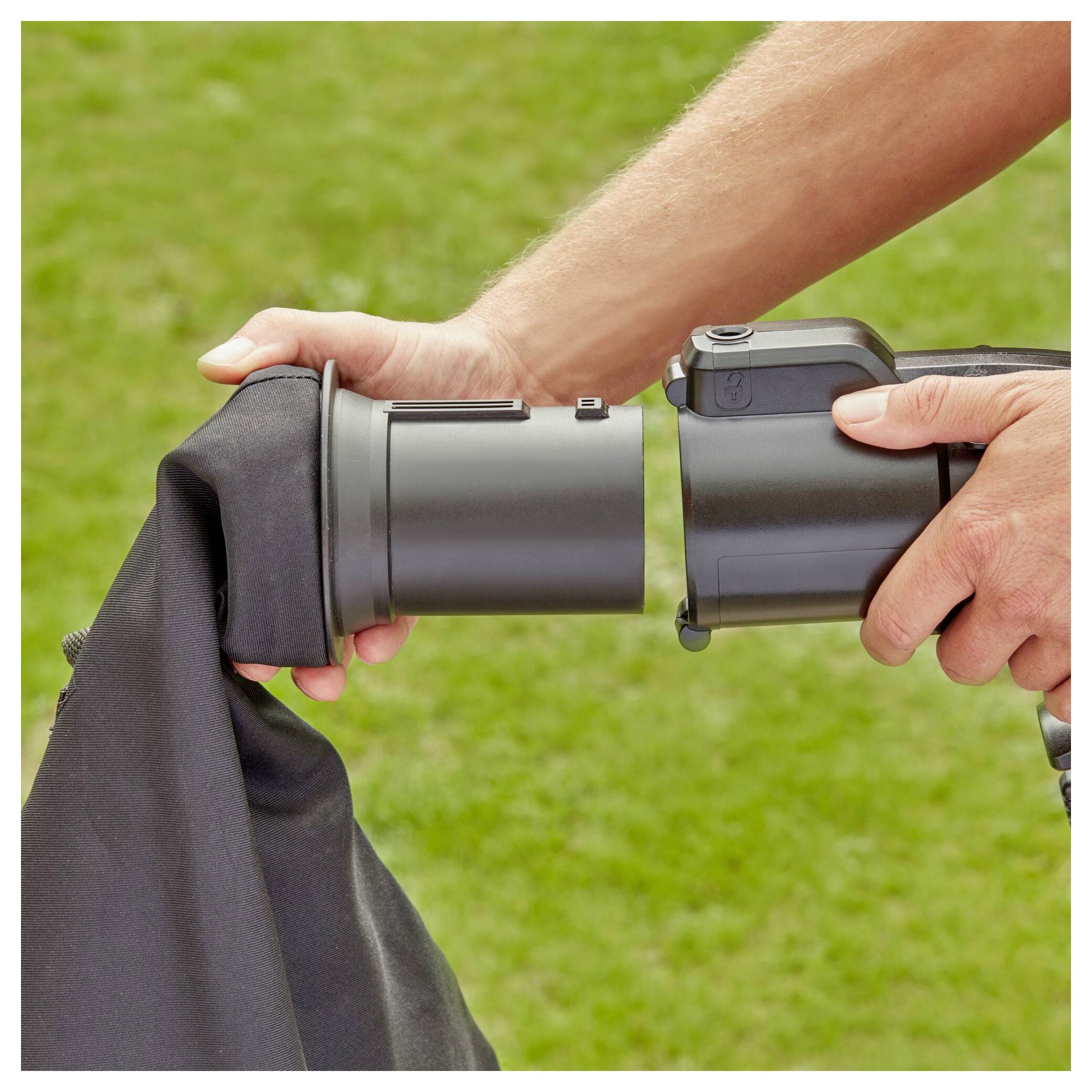 Eine Person zeigt, wie man Staubsäcke an einem Laubgebläse im Garten befestigt und demonstriert die richtige Ausrichtung der Teile für eine ordnungsgemäße Installation.