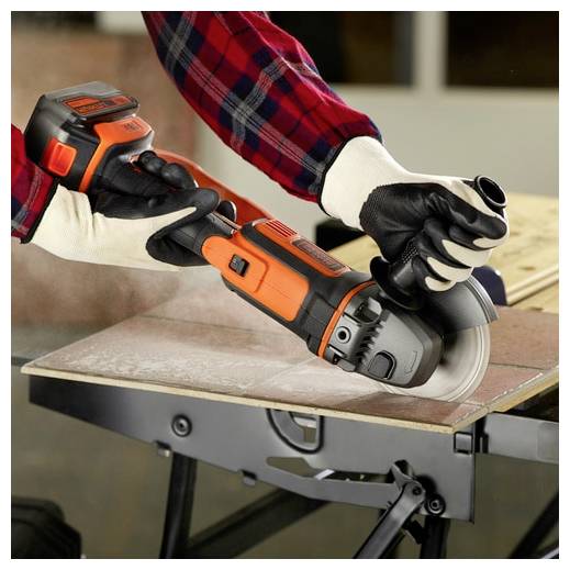 Eine Person, die ein orange-schwarzes Elektrowerkzeug verwendet, um eine Fliese auf einer Werkbank zu schneiden, trägt ein rotes Karohemd und Schutzhandschuhe.