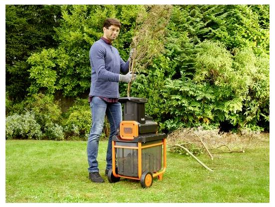 Eine Person, die einen elektrischen Häcksler verwendet, um Äste in einem Garten zu verarbeiten, umgeben von üppigem grünem Laub.