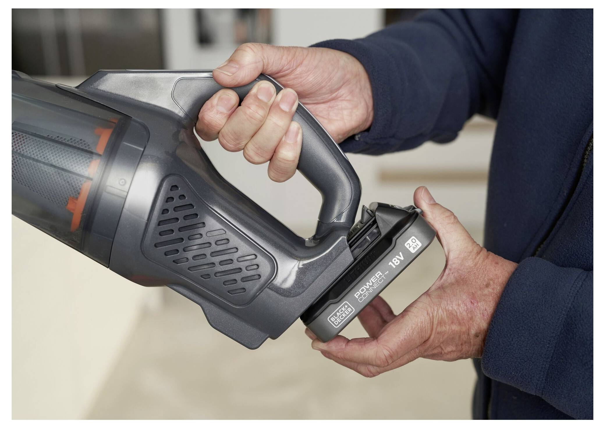 Eine Person setzt einen wiederaufladbaren Akku in einen tragbaren Staubsauger ein und demonstriert dabei die einfache Akku-Austauschbarkeit.