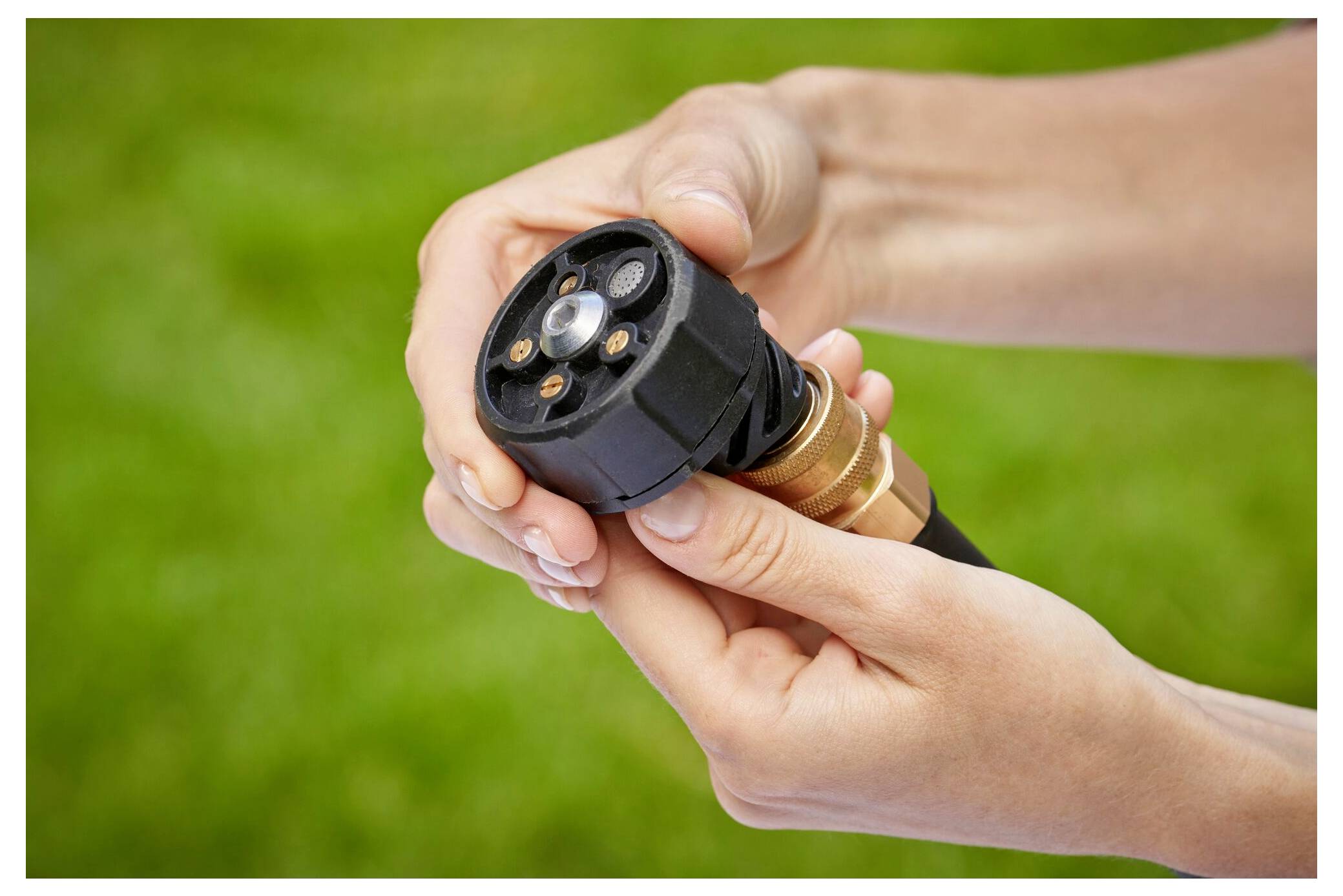 Zwei Hände, die eine Gartenschlauch-Düse einstellen, vor einem unscharfen grünen Hintergrund gehalten.