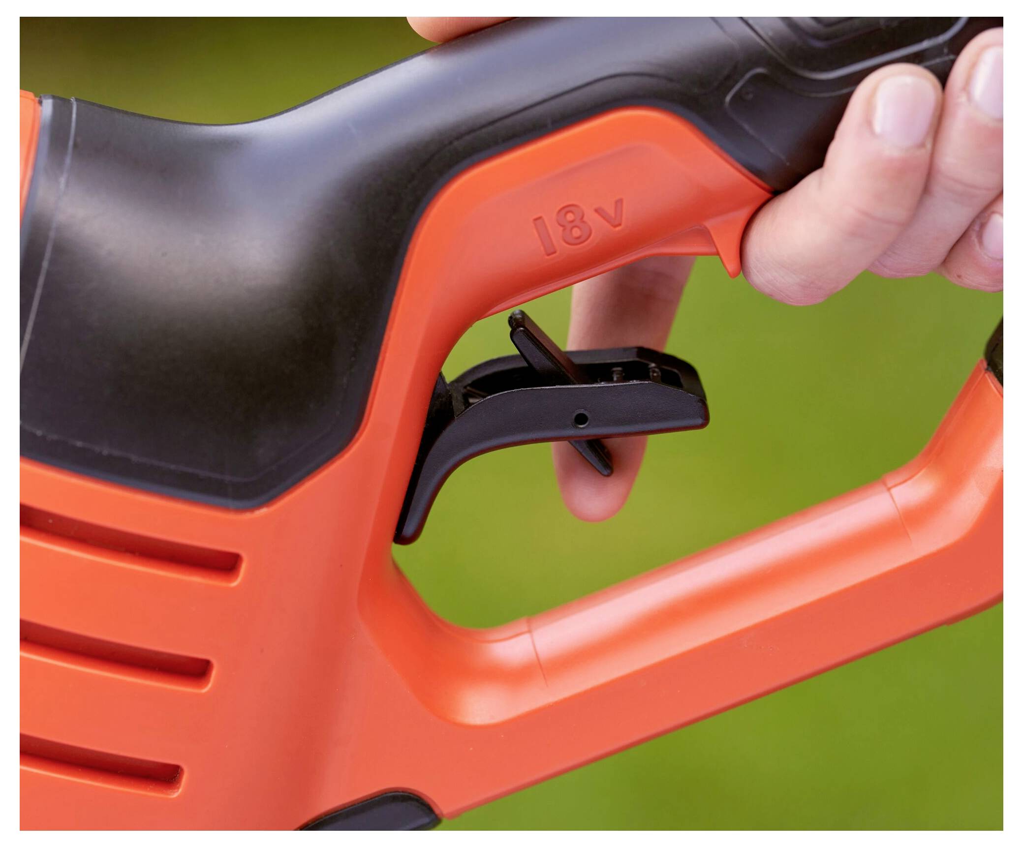 Eine Hand hält ein schwarzes und oranges 18-V-Elektrowerkzeug, wobei der Fokus auf dem Abzug und dem Griff vor einem grünen Hintergrund liegt.