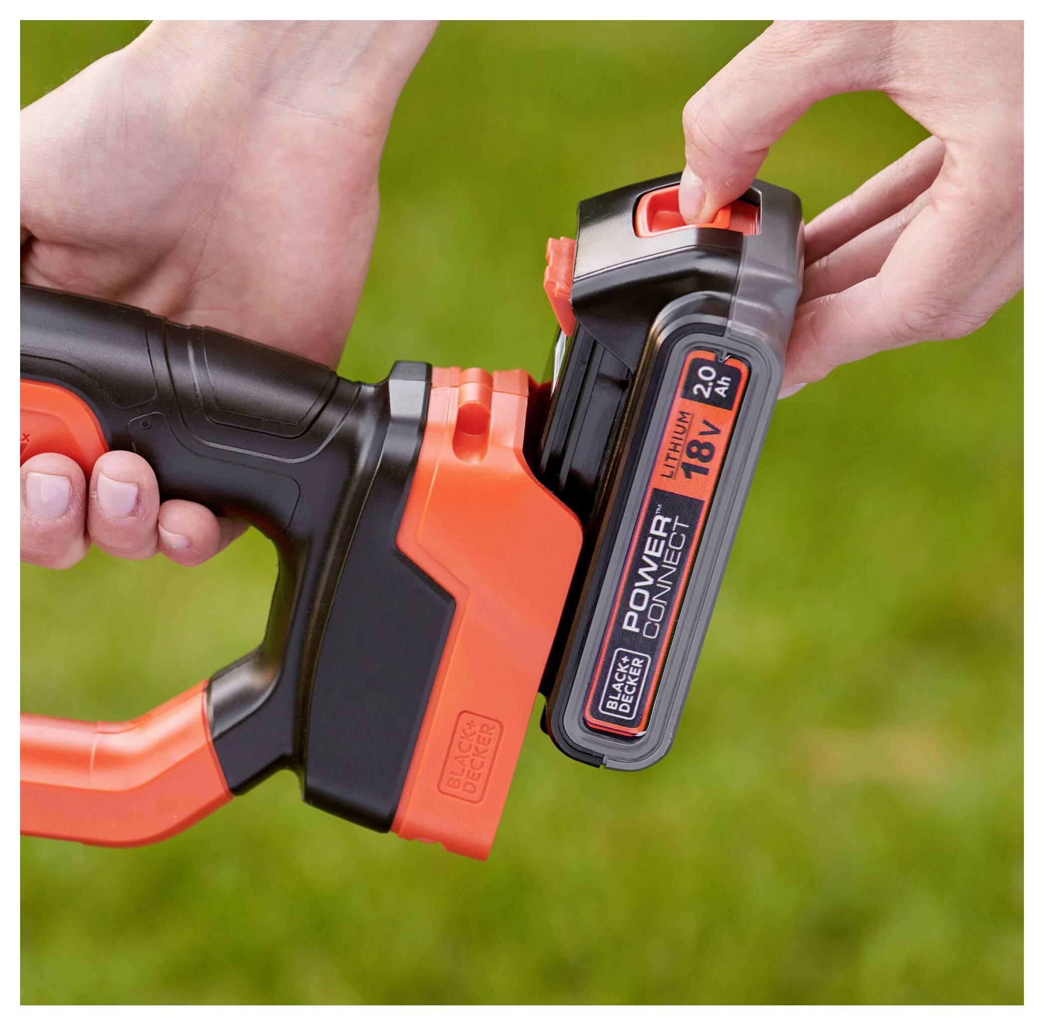 Nahaufnahme von Händen, die eine schwarze und orange 20V-Lithium-Batterie in ein Elektrowerkzeug-Griff im Freien einsetzen.