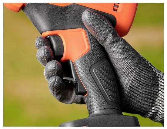 Eine behandschuhte Hand hält den Griff eines Elektrowerkzeugs und zeigt den Griff und den Auslöser, vor einem unscharfen Außenhintergrund.