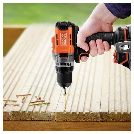 Eine Person verwendet einen Hochdruckwasserschlauch, um ein Fahrrad auf einer grasbewachsenen Fläche vor einer Holzstruktur zu waschen, umgeben von Grünflächen.