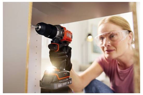 Eine Person mit einer Schutzbrille benutzt einen schnurlosen Bohrer, um eine Schraube in eine Holzoberfläche zu befestigen, was auf Heimwerker- oder DIY-Aktivitäten hinweist.