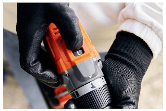 Eine Person mit schwarzen Handschuhen stellt die Einstellung an einem orange-grauen Elektrowerkzeug ein und konzentriert sich auf Präzision und Kontrolle in einer Arbeitsumgebung.