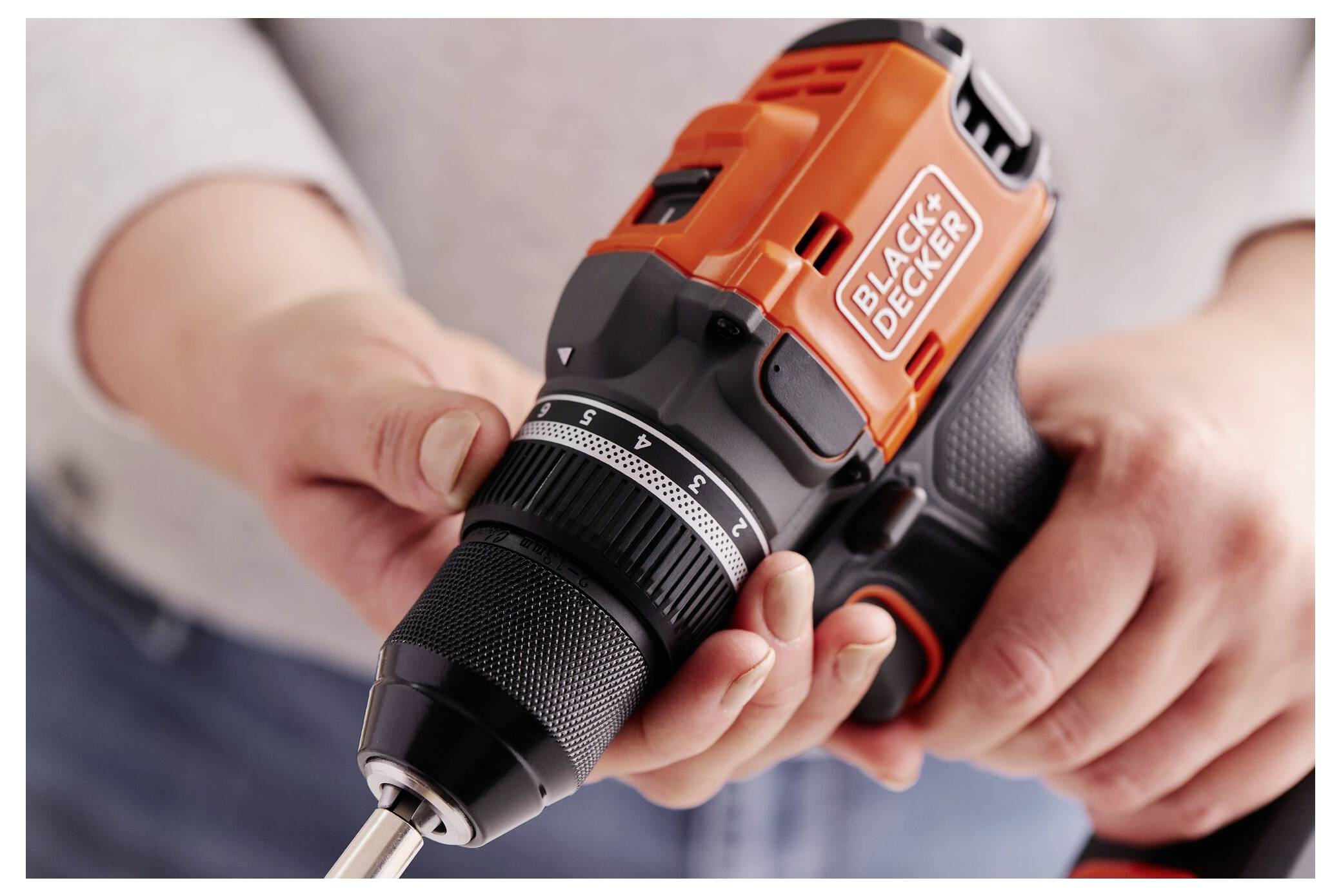 Eine Person hält einen schnurlosen Black & Decker Bohrer und stellt dessen Einstellungen ein, wobei die Benutzerfreundlichkeit und der Griff betont werden.