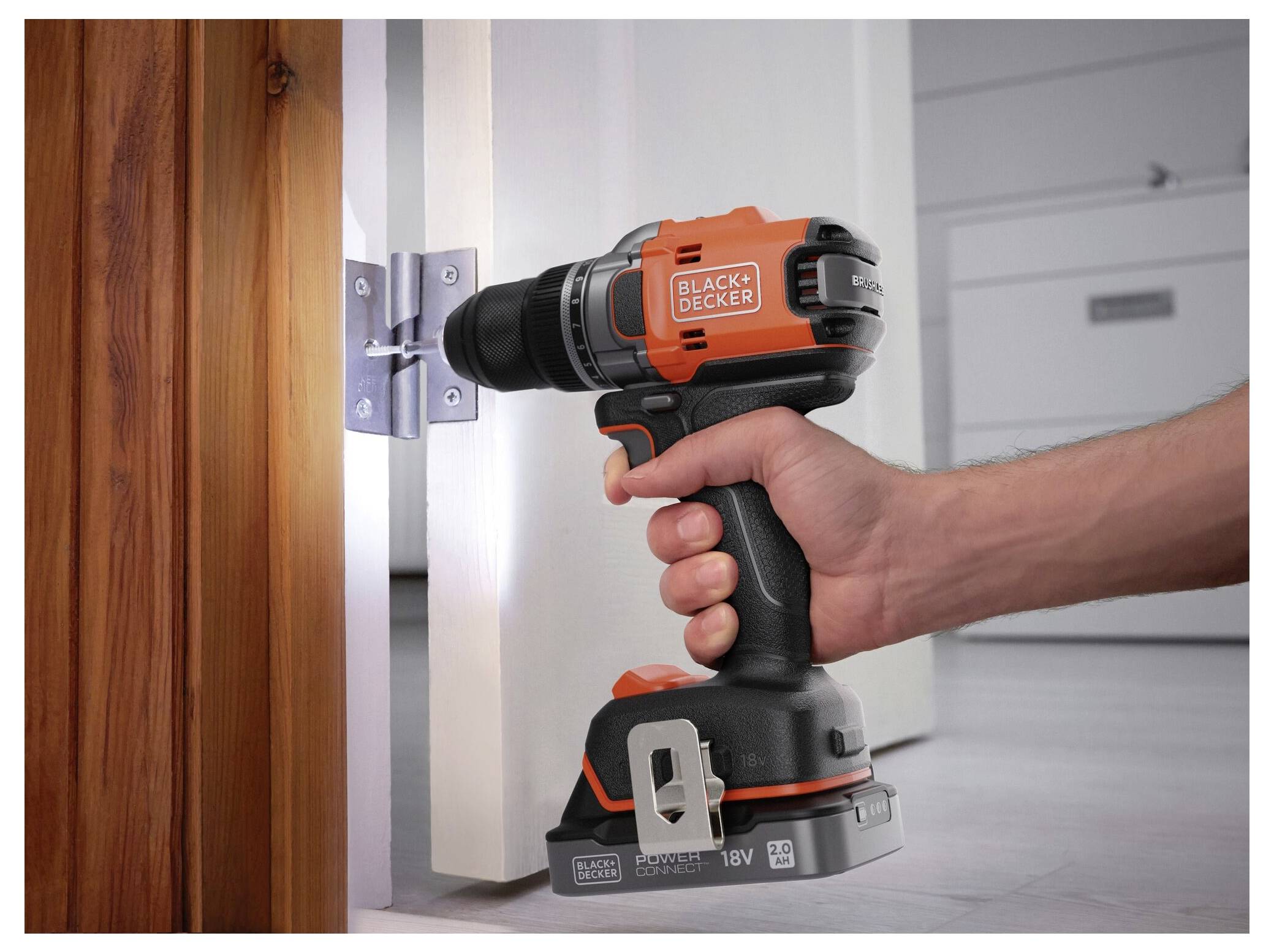 Eine Person benutzt einen orange-schwarzen kabellosen Bohrer, um ein Scharnier an einer Holztür zu befestigen.