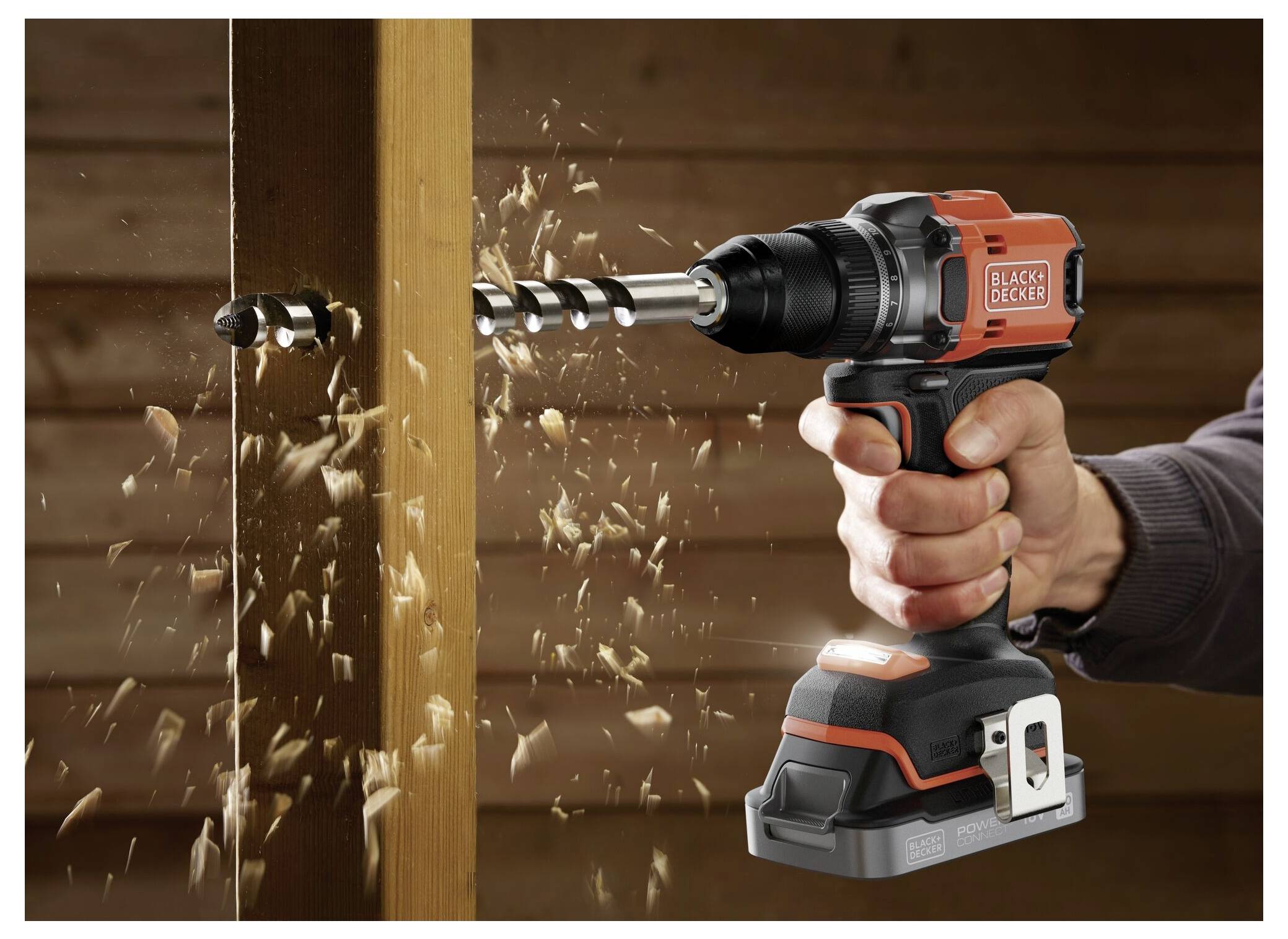 „Hand, die einen kabellosen Black & Decker Elektroschrauber hält, bohrt in ein Holzbrett, wobei Holzspäne herumfliegen.