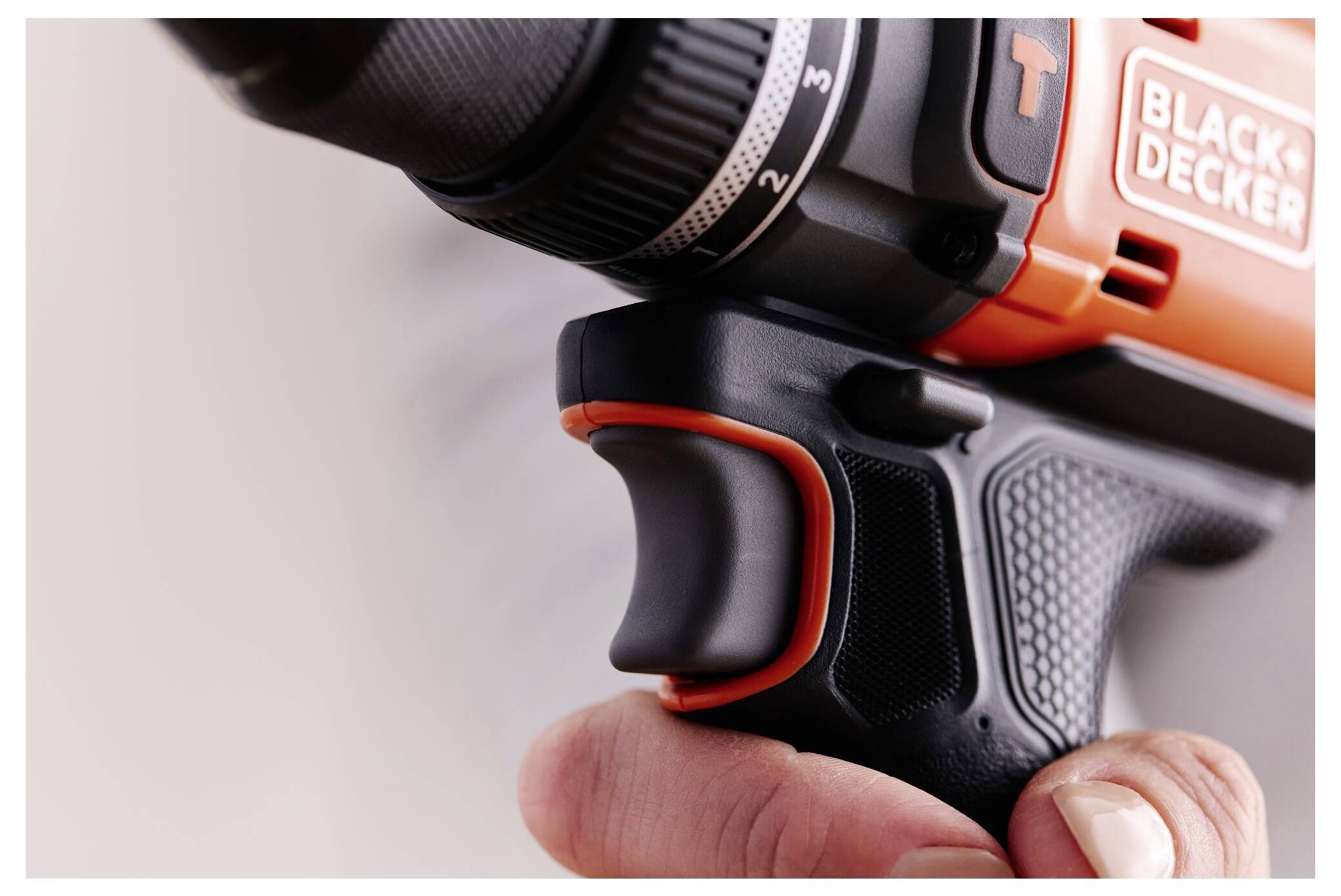 Nahaufnahme einer Hand, die einen orange-schwarzen Bohrer hält, mit Fokus auf den Griff und den Auslösebereich, wobei ein Teil eines Logos sichtbar ist.