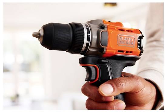 Eine Person hält einen orange-schwarzen kabellosen Bohrer der Marke „BLACK+DECKER