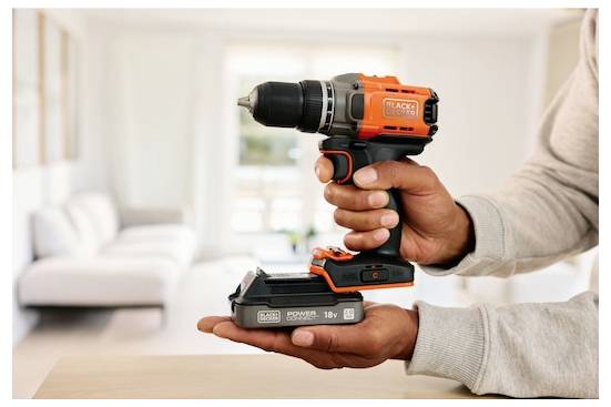 Eine Person hält einen orange-schwarzen kabellosen Bohrer in einem hellen Raum und zeigt sein kompaktes Design und seine 18-V-Leistungsfähigkeit.