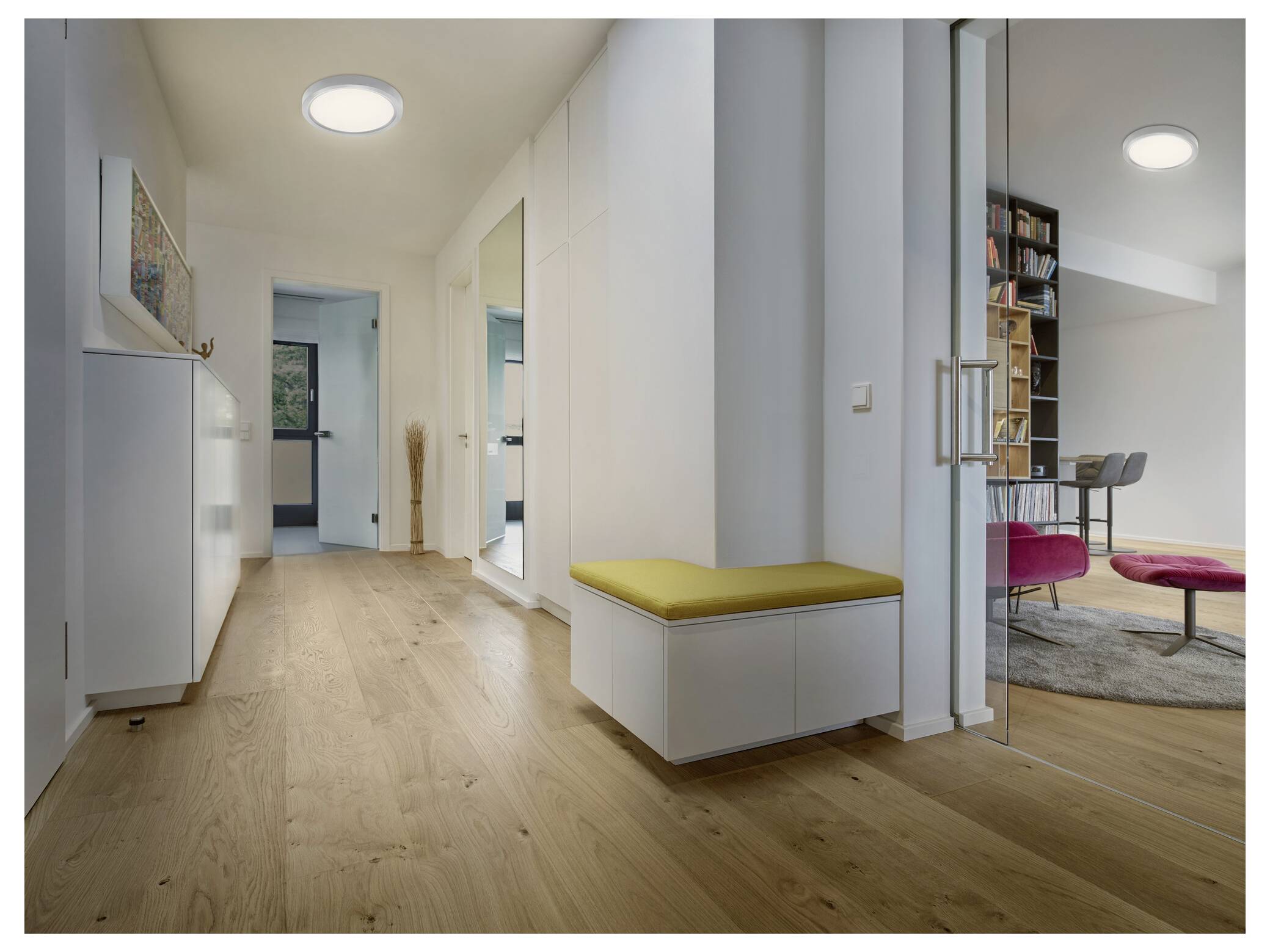 Eine Person, die einen Karton trägt, geht durch einen hell beleuchteten Flur mit sechseckig gefliesten Böden.