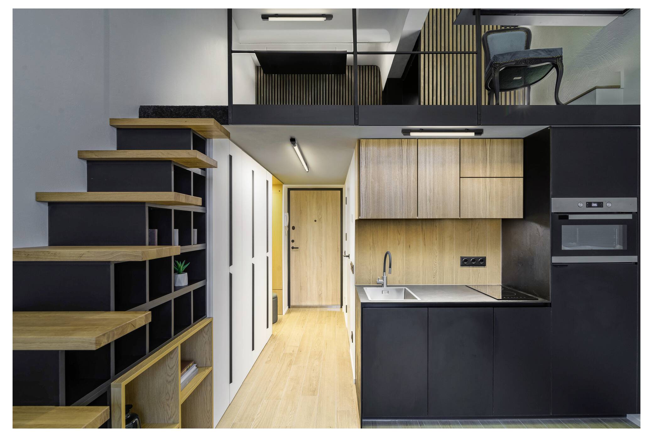 Ein modernes Loft-Apartment mit einer Holztreppe führt zu einem oberen Loft-Bereich. Die Hauptebene verfügt über eine kompakte Küche mit schwarzen Schränken und Holzschränken.