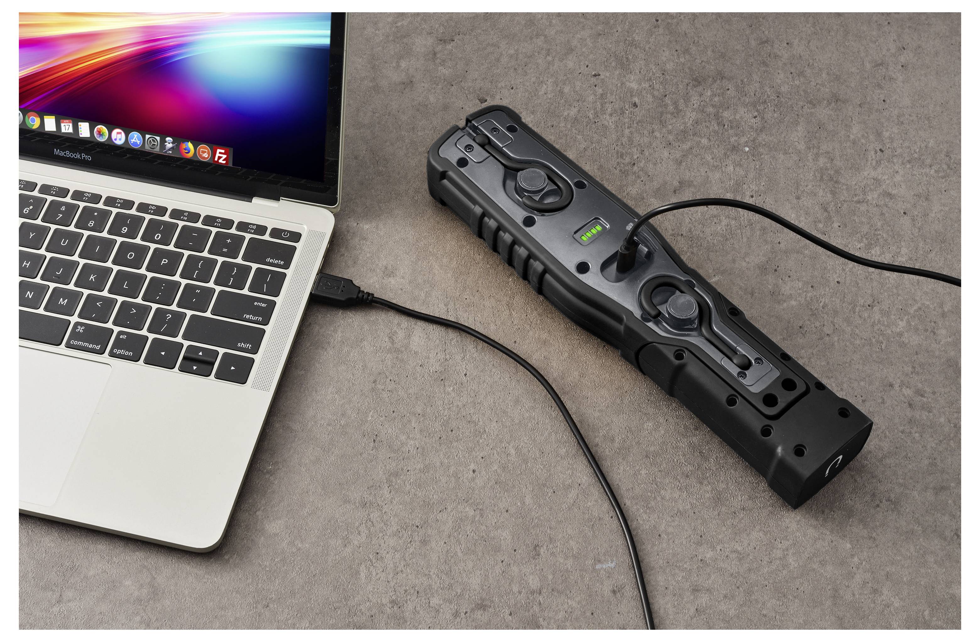 Laptop, der über ein Kabel mit einer schwarzen tragbaren Stromstation auf einer Tischplatte verbunden ist, wobei die Anzeigelampe der Powerbank eingeschaltet ist.