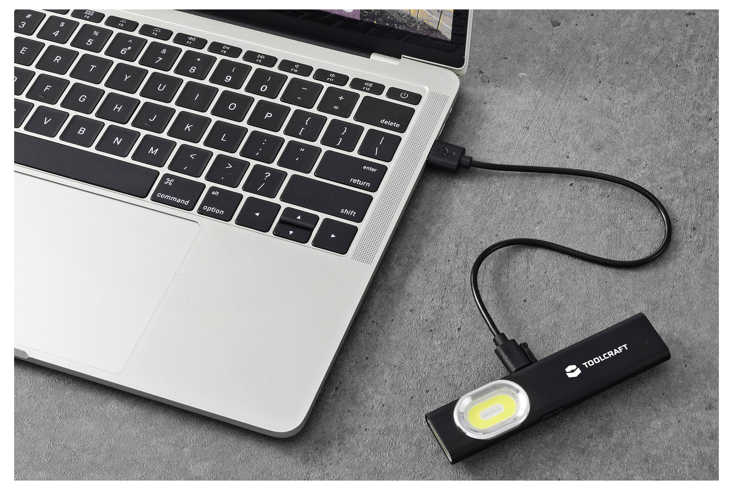 USB-aufladbare Arbeitsleuchte, die über ein Kabel an einen Laptop angeschlossen ist, auf einer grauen Tischplatte dargestellt.