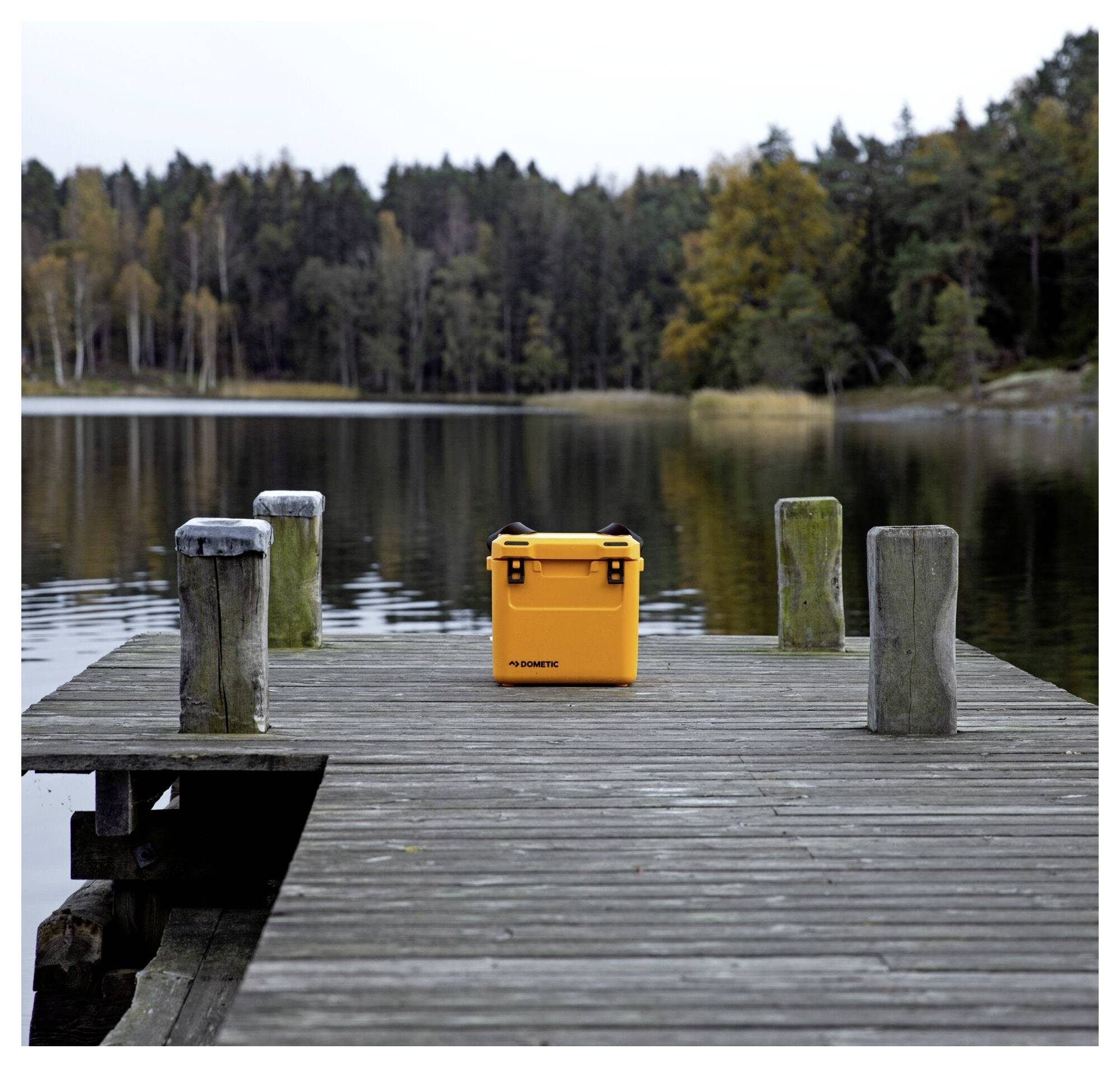 Orangefarbener Kühlbox auf einem Holzsteg neben einem ruhigen Waldsee.