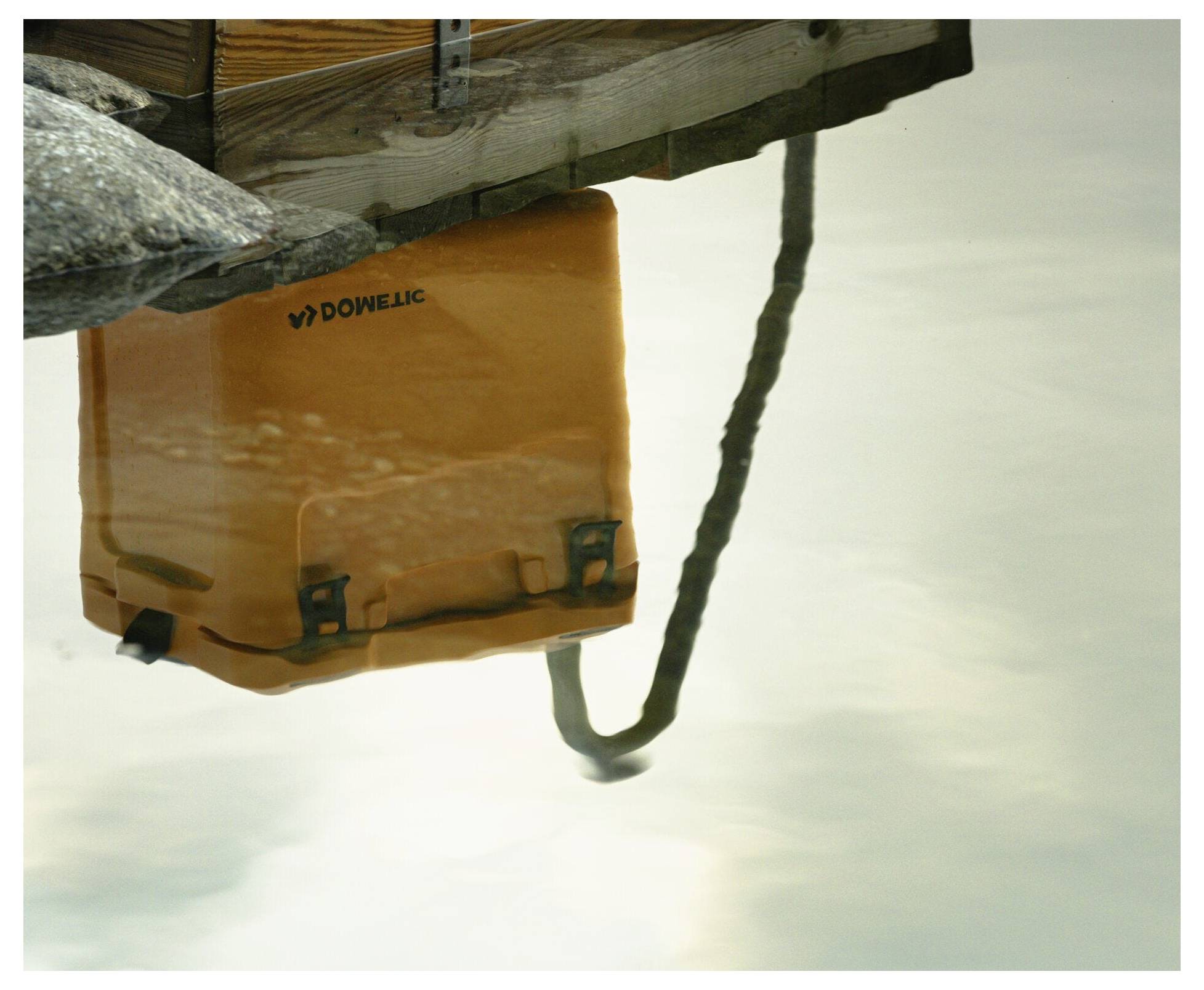 Orange DOWELLC Schwimmbeutel spiegelt sich in ruhigem Wasser neben einer Dockante und einem Seil.