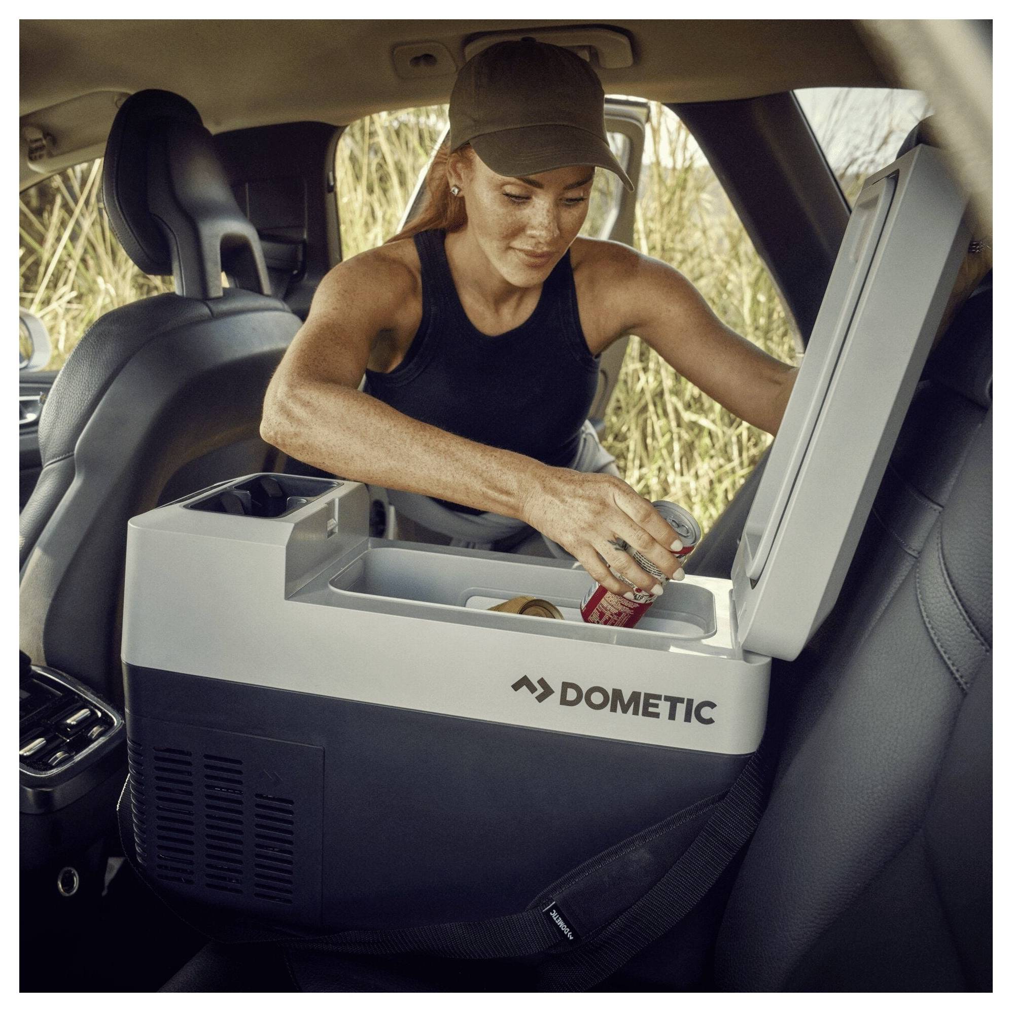 Eine Frau in einem Fahrzeug greift in eine tragbare Dometic-Kühlbox hinein und legt ein Getränk hinein, während der Deckel offen ist.